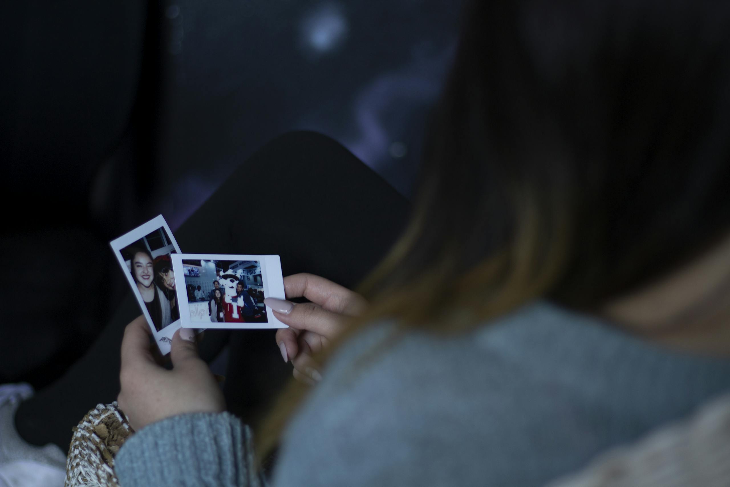 A woman sits indoors reminiscing while holding nostalgic Polaroid photos.
